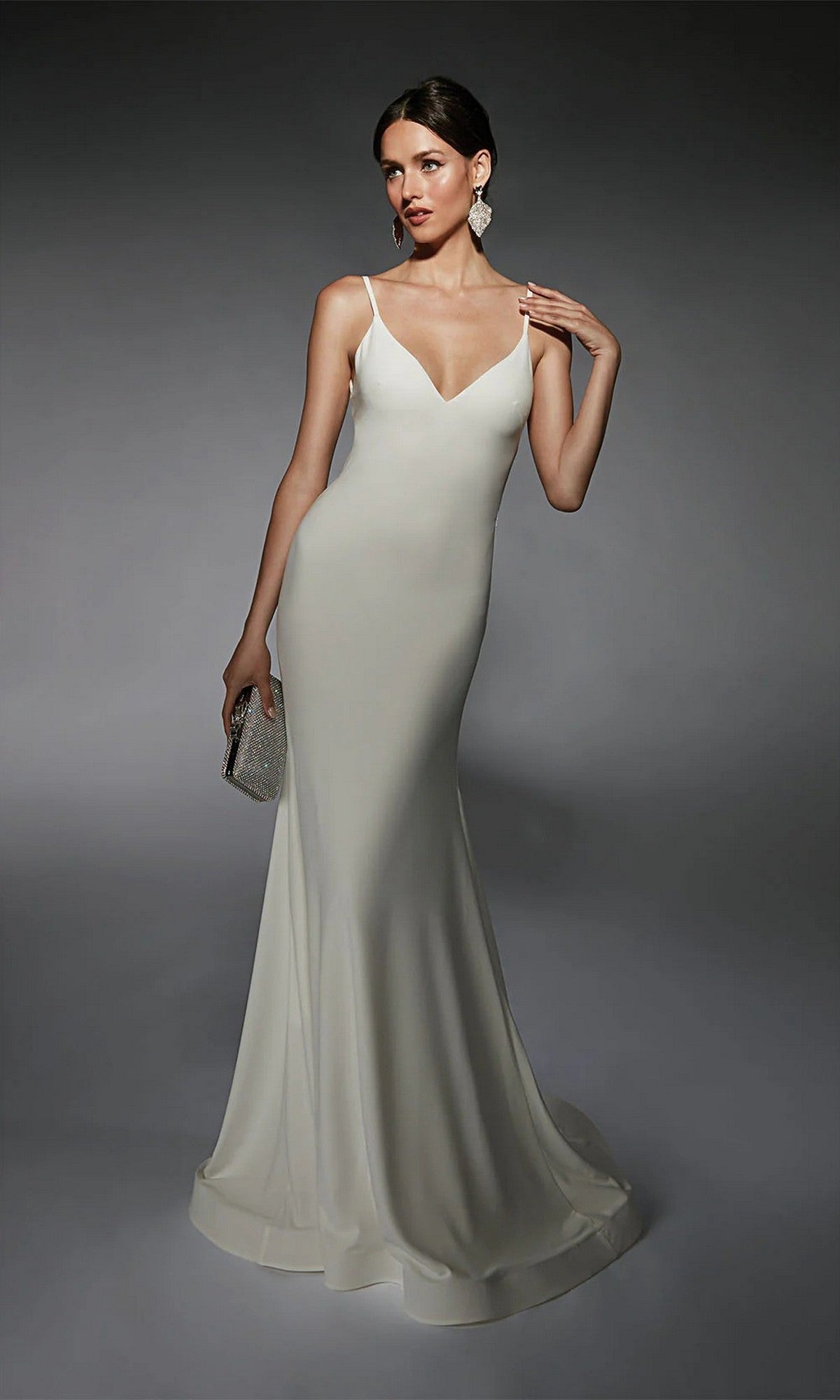 A woman models the Alyce 7108 long white dress—fitted, sleeveless, floor-length with thin straps—holding a small clutch and posing against a gray background.